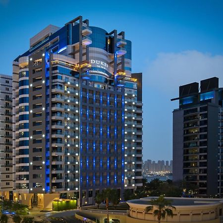 Dukes The Palm, A Royal Hideaway Hotel Dubai Exterior foto The photo shows a modern high-rise building, which appears to be a hotel or residential complex. The design features sleek lines and a glass façade, illuminated with blue lighting that enhances its contemporary look. Surrounding the main building are