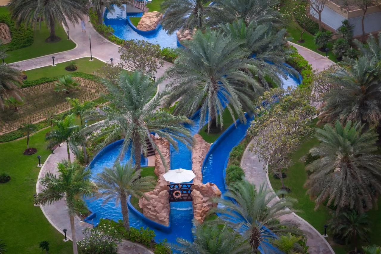 Dukes The Palm, A Royal Hideaway Hotel Dubai Exterior foto The photo shows a beautifully landscaped outdoor area featuring a winding water channel with vibrant blue water. Flanking the waterway are lush green palm trees and other vegetation, creating a tropical ambiance. There are also stone features along t