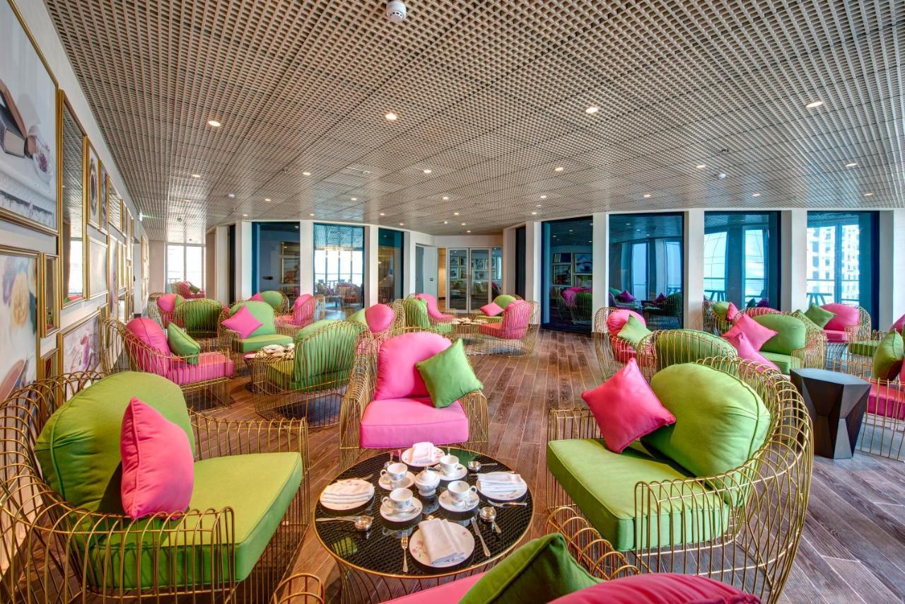 Dukes The Palm, A Royal Hideaway Hotel Dubai Exterior foto The photo shows a stylish and modern lounge area. The seating consists of unique chairs and sofas that combine bright green and pink colors, adorned with matching cushions. The space has a contemporary design, featuring a wooden floor and large windo