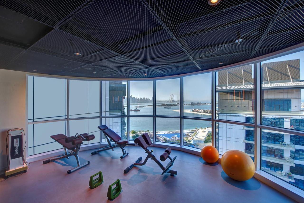 Dukes The Palm, A Royal Hideaway Hotel Dubai Exterior foto The photo shows a modern gym or fitness area that features large windows with a view of a waterfront and skyline. Inside, there are several pieces of fitness equipment, including adjustable benches and exercise balls. The design is sleek and contempo