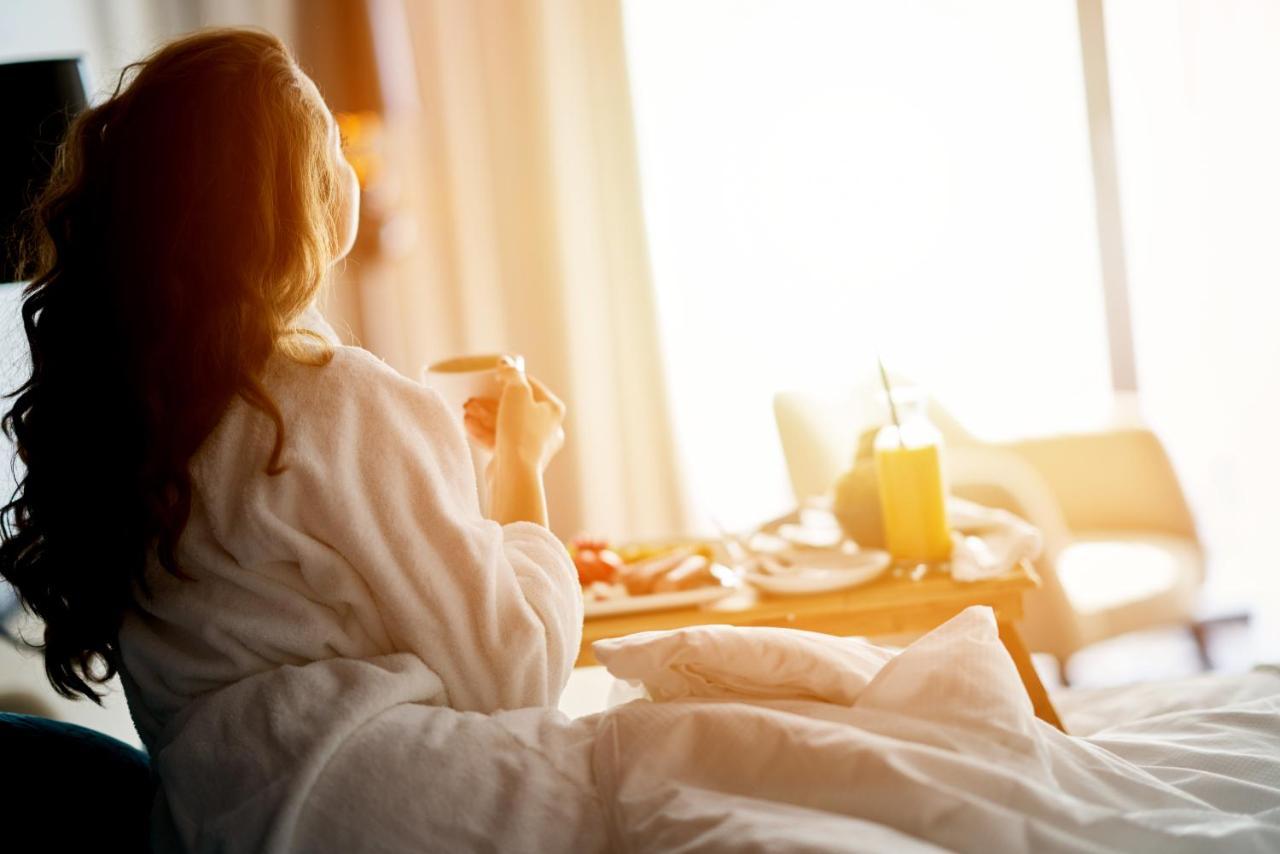 Dukes The Palm, A Royal Hideaway Hotel Dubai Exterior foto The image shows a person sitting on a bed, wearing a cozy bathrobe. They appear to be enjoying a moment of relaxation, possibly sipping a drink from a cup. In front of them, there is a tray with food and a drink, suggesting a breakfast or brunch setu