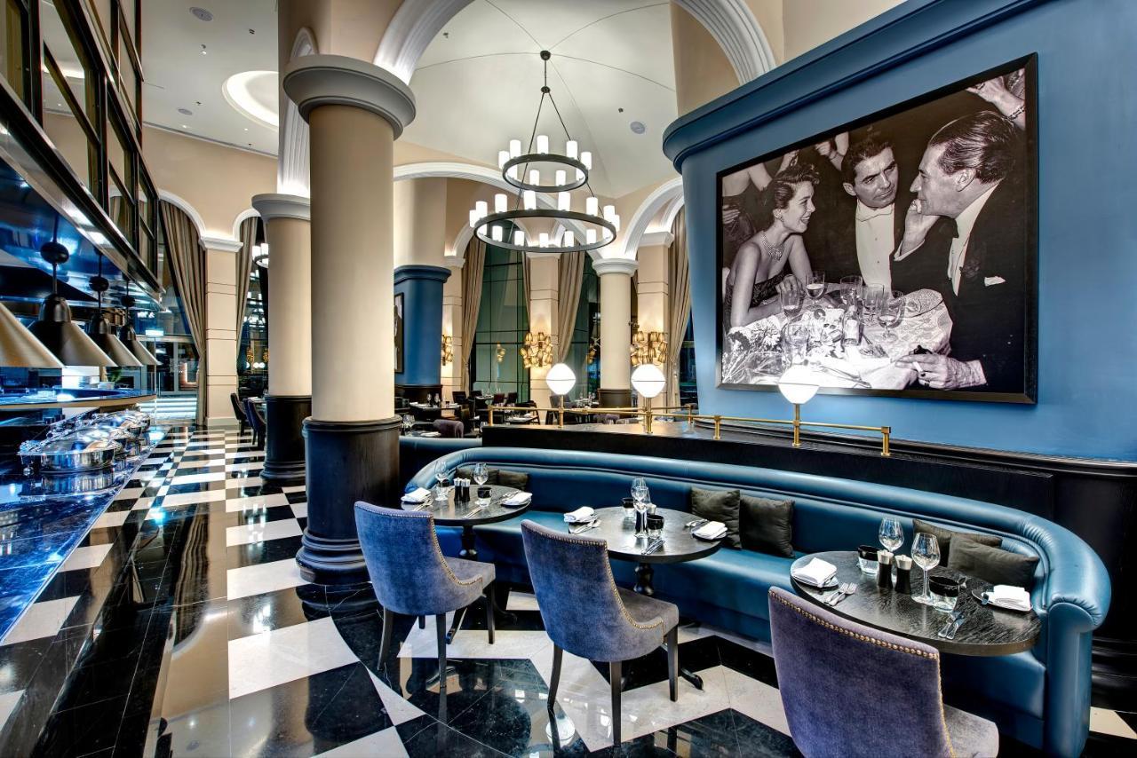 Dukes The Palm, A Royal Hideaway Hotel Dubai Exterior foto The image shows an elegant restaurant interior with a sophisticated design. The space features high ceilings, large columns, and a combination of blue and black color schemes. There is a stylish seating area with upholstered chairs and tables set for