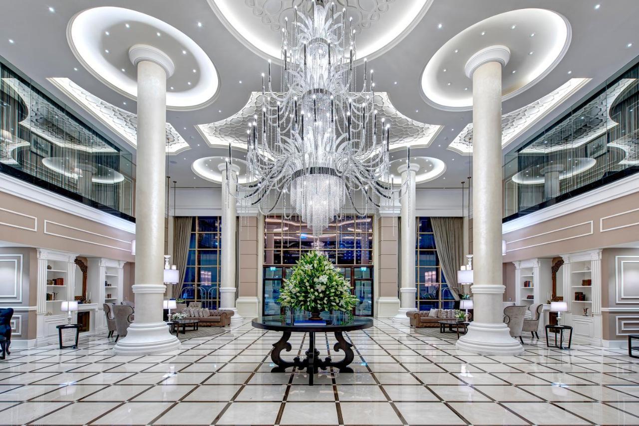 Dukes The Palm, A Royal Hideaway Hotel Dubai Exterior foto The photo depicts the interior of a luxurious lobby or hotel entrance. It features tall, elegant columns and a grand chandelier hanging from the ceiling, illuminating the space with soft light. The floor is tiled with a geometric pattern, enhancing t