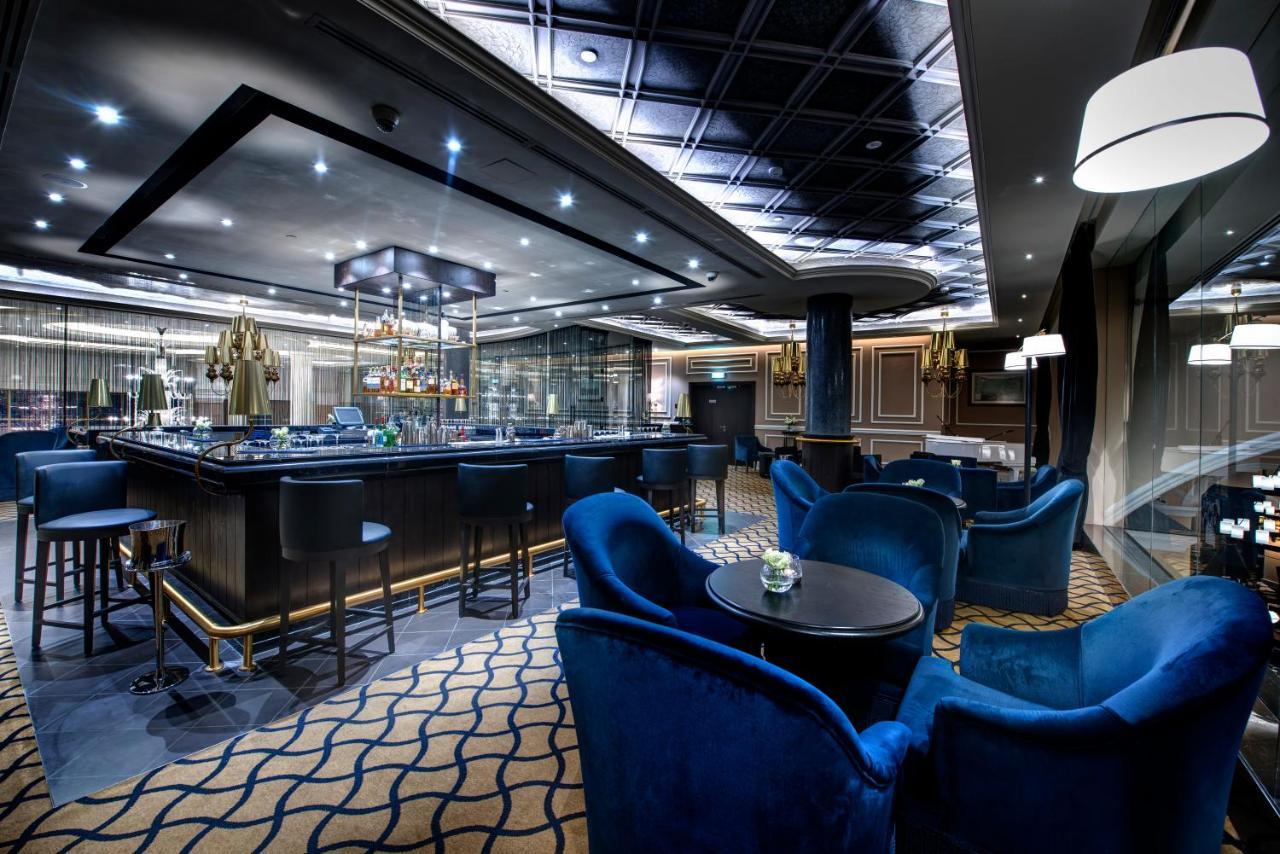 Dukes The Palm, A Royal Hideaway Hotel Dubai Exterior foto The photo shows an upscale bar or lounge area. The interior features modern design elements with elegant lighting. There is a stylish bar counter with a variety of drinks, and seating consists of plush blue armchairs arranged around small tables. The