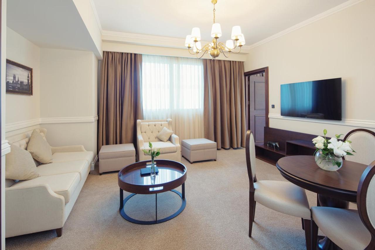 Dukes The Palm, A Royal Hideaway Hotel Dubai Exterior foto The photo shows a well-furnished living space. There is a light-colored sofa, a comfortable armchair, and an ottoman, arranged around a round wooden coffee table. A dining table with chairs is also present. The room features a large window draped wit