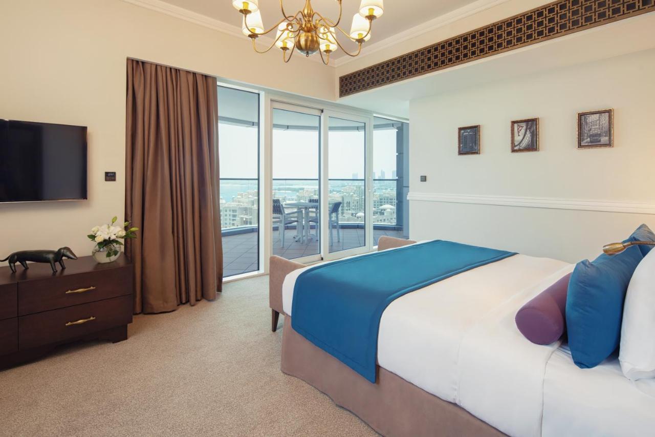 Dukes The Palm, A Royal Hideaway Hotel Dubai Exterior foto The photo shows a stylish and modern bedroom. It features a large bed with a blue and purple throw blanket, complemented by decorative pillows. Next to the bed, there is a dark wooden nightstand. A flat-screen TV is mounted on the wall opposite the b