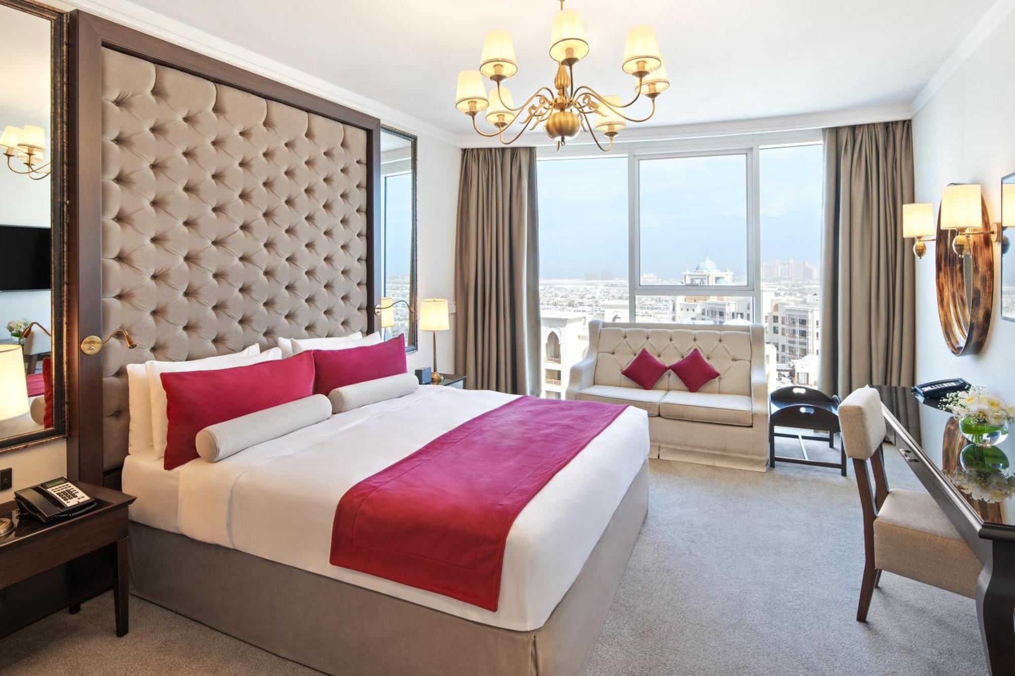 Dukes The Palm, A Royal Hideaway Hotel Dubai Exterior foto The photo shows a luxurious hotel room featuring a large, well-made bed with a plush headboard. The bed is adorned with decorative cushions, primarily in shades of red. There is a stylish sofa nearby, also featuring similar color accents. The room is