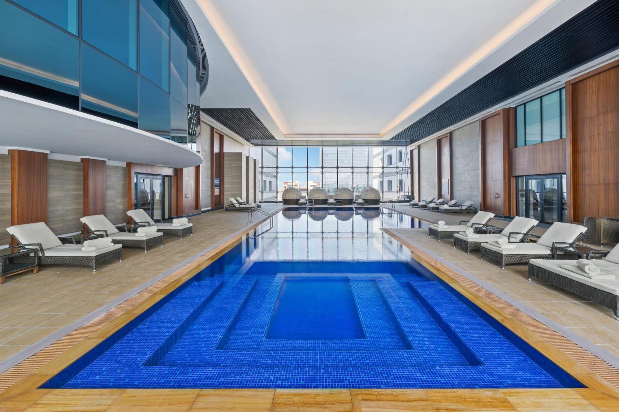 Dukes The Palm, A Royal Hideaway Hotel Dubai Exterior foto The photo shows a modern indoor swimming pool area. The pool itself is a deep blue color and has a rectangular shape, featuring a smaller inset section. Surrounding the pool, there are lounge chairs arranged neatly, likely for relaxation. The space i
