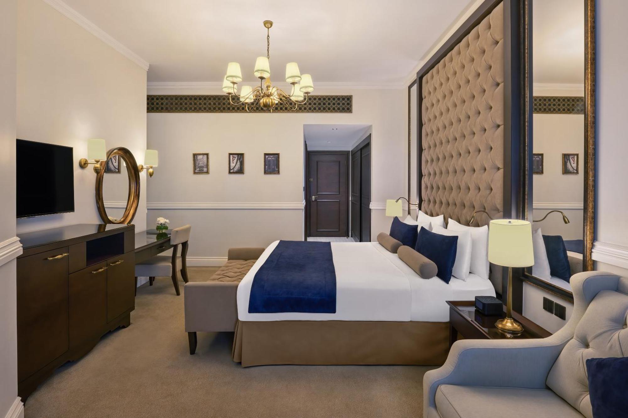 Dukes The Palm, A Royal Hideaway Hotel Dubai Exterior foto The photo shows a stylish hotel room. It features a large bed with white linens and a blue throw blanket, which is placed against a luxurious padded wall. On either side of the bed, there are bedside lamps. A modern chandelier hangs from the ceiling,