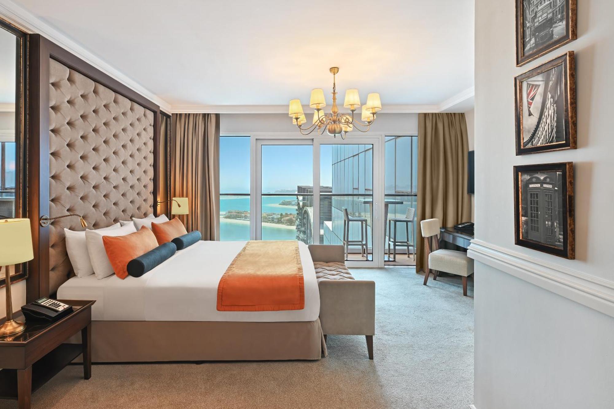 Dukes The Palm, A Royal Hideaway Hotel Dubai Exterior foto The photo shows a luxurious hotel room featuring modern decor. The room includes a large bed with a tufted headboard, adorned with orange and black accent pillows. There are large windows that offer a view of the outdoors, with sheer curtains and dar