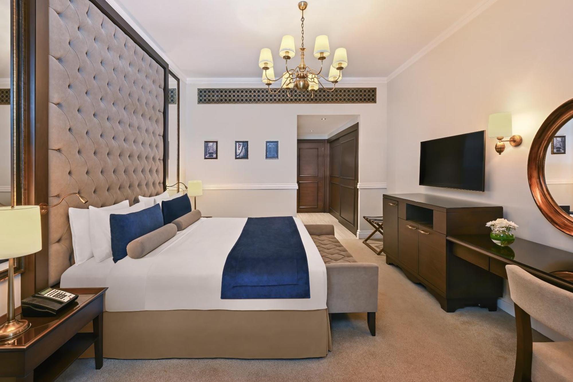 Dukes The Palm, A Royal Hideaway Hotel Dubai Exterior foto The image shows a hotel room featuring a large, neatly arranged bed with decorative pillows. The headboard is tufted and upholstered in a beige fabric. There is a small sofa or bench at the foot of the bed in a contrasting color. The room is well-lit