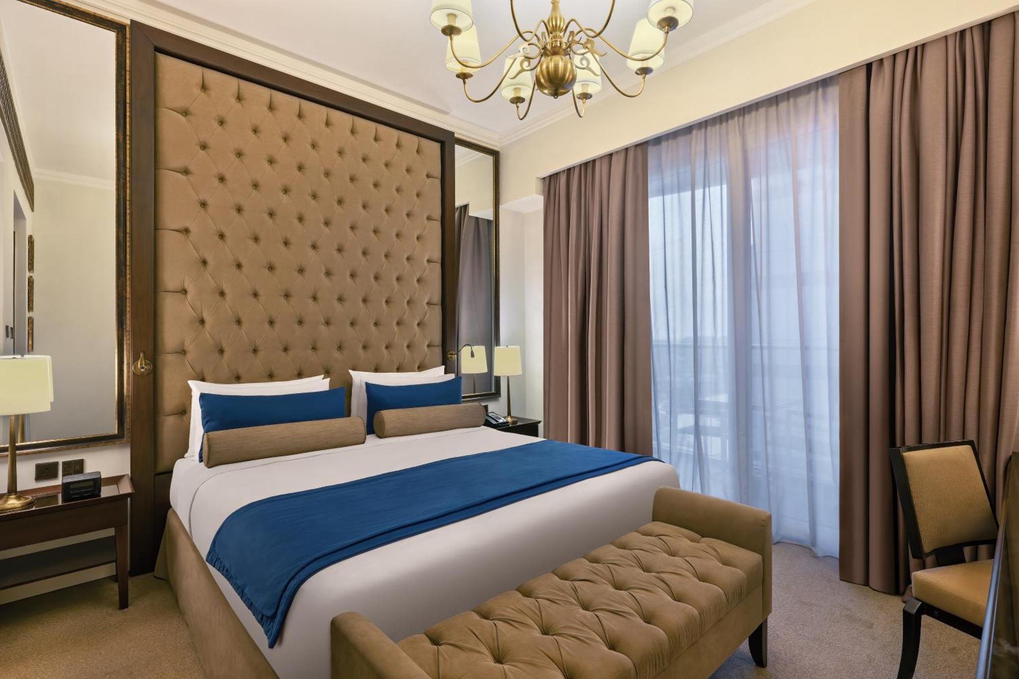 Dukes The Palm, A Royal Hideaway Hotel Dubai Exterior foto The photo depicts a stylish hotel room with a modern design. It features a large bed with a tufted headboard upholstered in a tan color. The bed is dressed with white sheets and dark blue and beige decorative pillows. On either side of the bed, there
