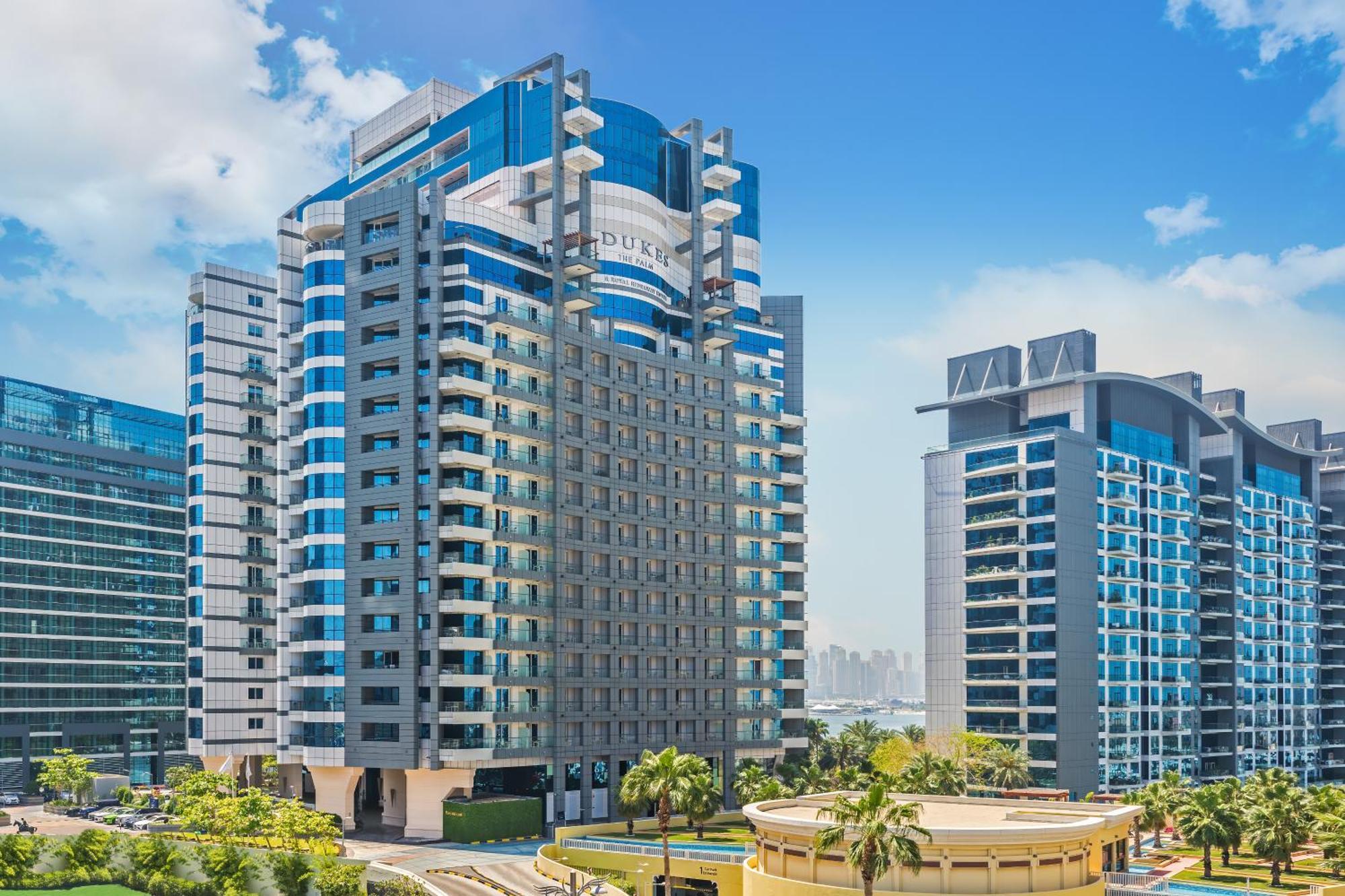 Dukes The Palm, A Royal Hideaway Hotel Dubai Exterior foto The photo depicts a modern urban skyline featuring several high-rise buildings. Prominent in the foreground is a sleek, multi-story structure with a combination of glass and concrete elements, showcasing a contemporary architectural style. The buildi
