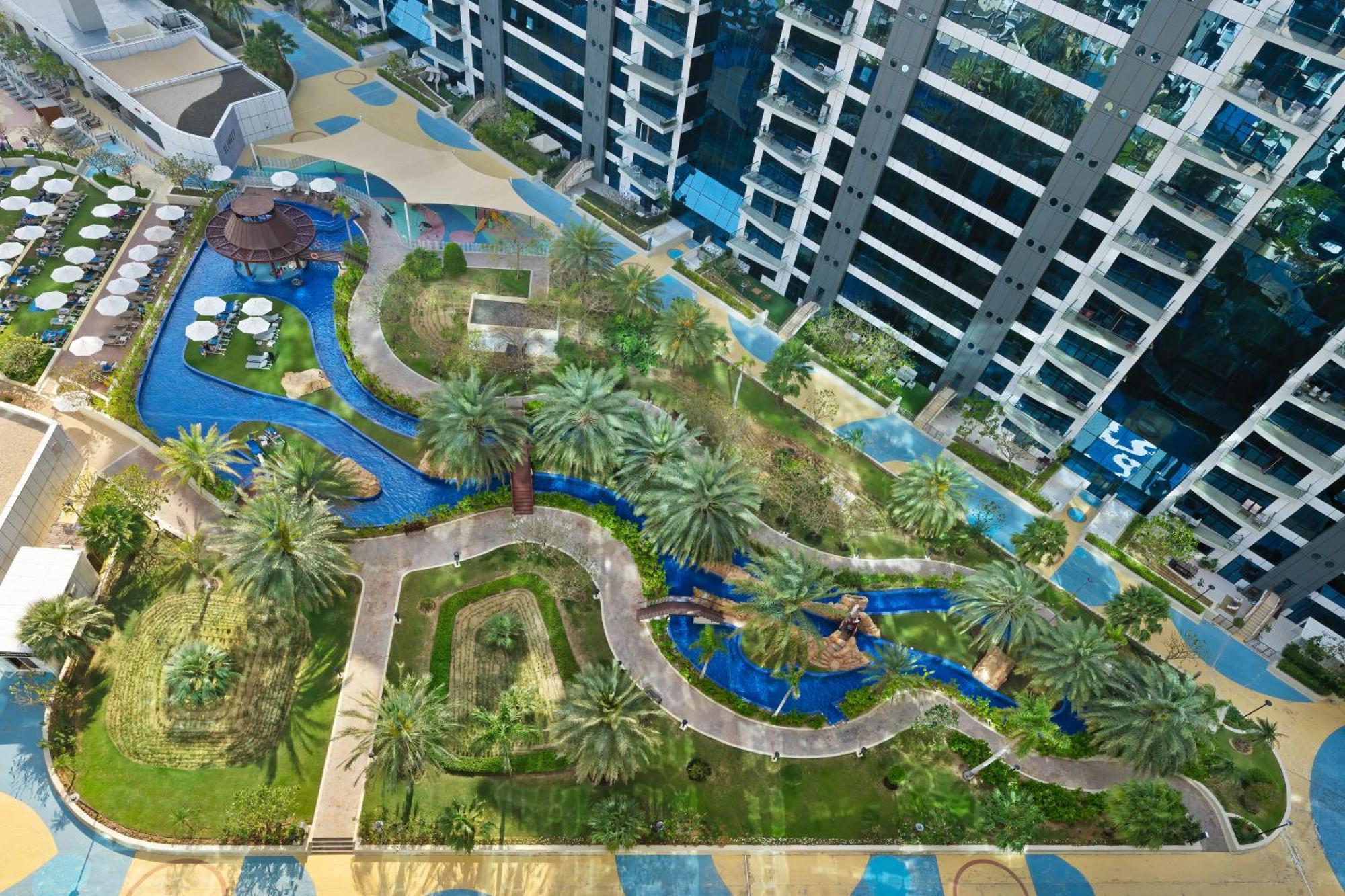 Dukes The Palm, A Royal Hideaway Hotel Dubai Exterior foto The photo showcases a landscaped area featuring a winding waterway that meanders through a garden-like setting. Surrounding the water are patches of greenery, including palm trees and various plants. There are pathways lined with tiles, and several c