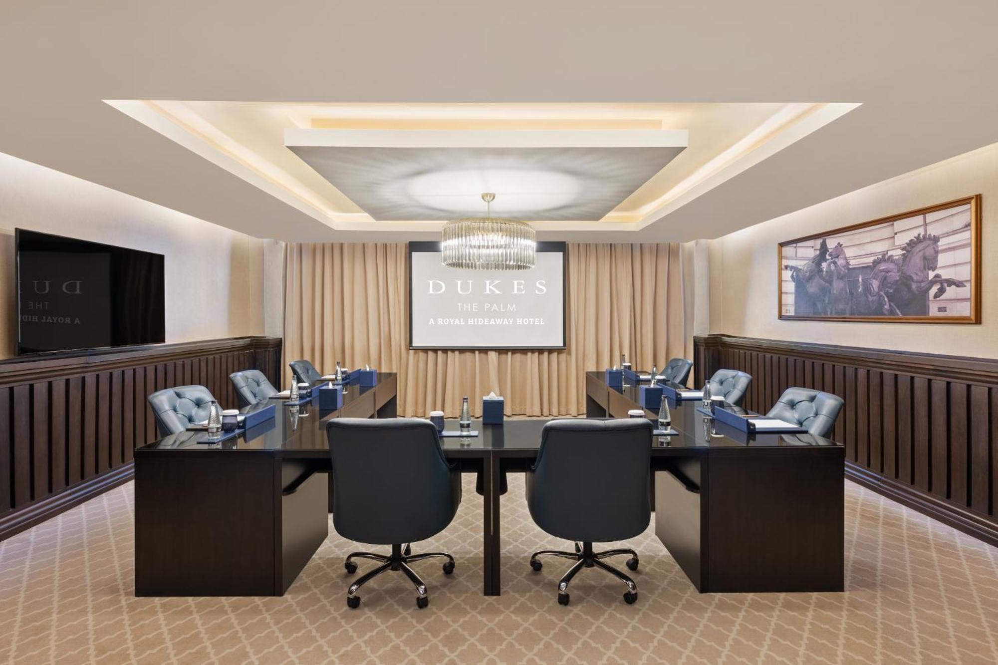 Dukes The Palm, A Royal Hideaway Hotel Dubai Exterior foto The photo shows a modern conference room designed for meetings. It features a large rectangular table in the center surrounded by several ergonomic chairs. On one side, there is a large projection screen displaying the word "DUKES." The room has eleg