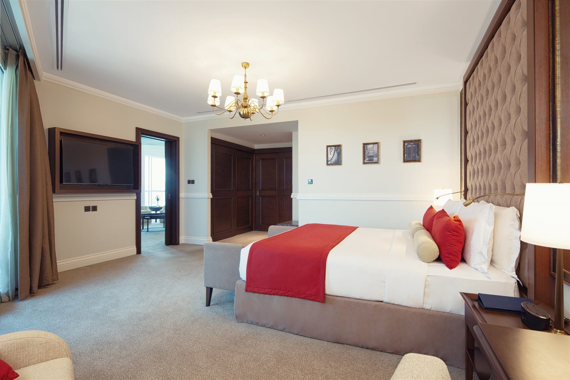 Dukes The Palm, A Royal Hideaway Hotel Dubai Exterior foto The photo shows a well-appointed hotel room. It features a large bed with white linens and red accent pillows. There is a comfortable seating area with a chair, and a side table. A chandelier hangs from the ceiling, providing lighting. On the wall be