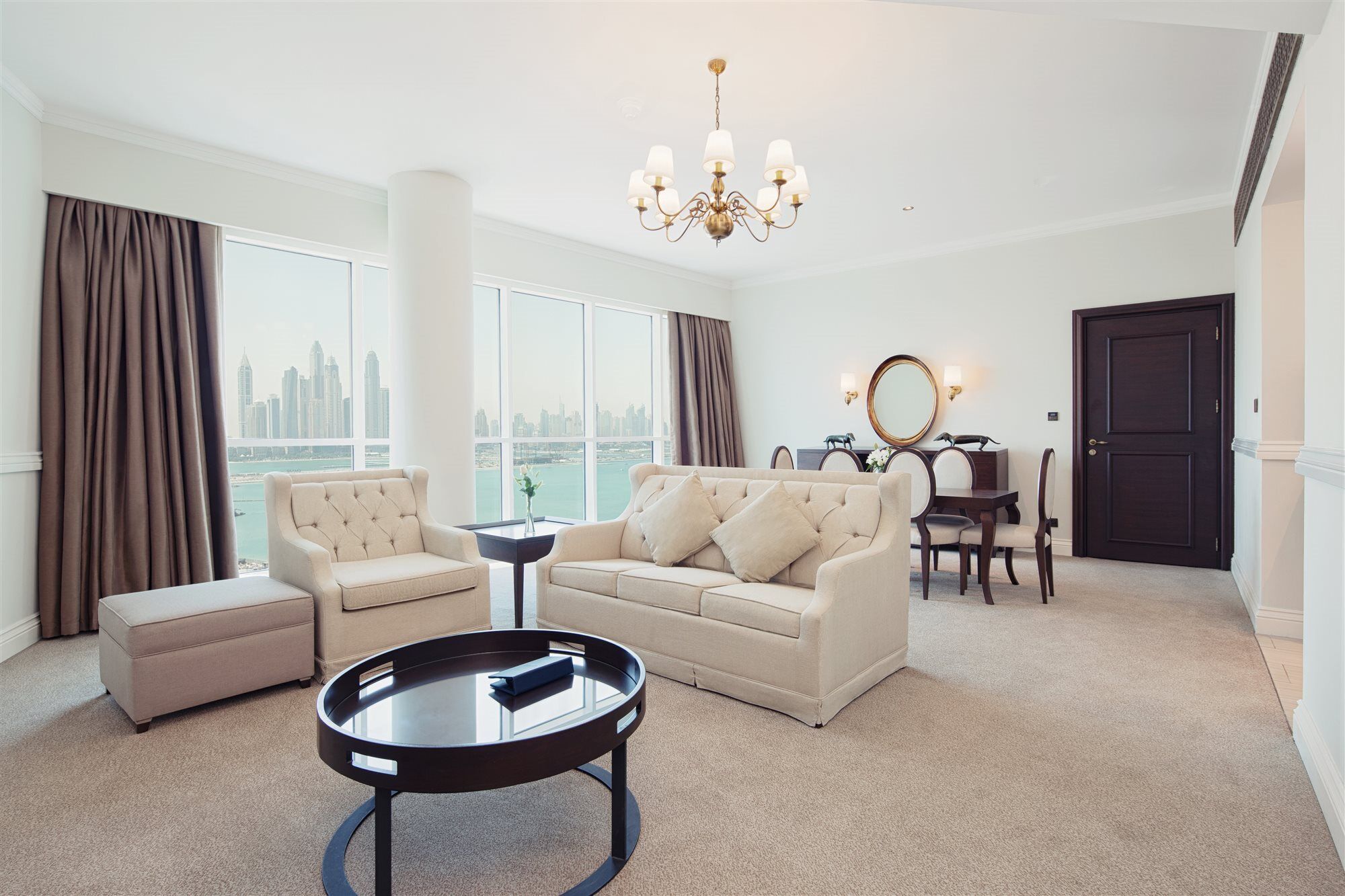 Dukes The Palm, A Royal Hideaway Hotel Dubai Exterior foto The photo shows a stylish and modern living room. It features a comfortable light-colored sofa with decorative cushions, a round black coffee table in the center, and a small matching stool nearby. There are large windows with views of a city skyline